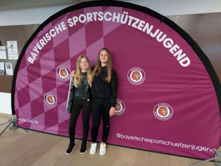 Zwei jugendliche Schützinnen vor einem Banner der Bayerischen Sportschützenjugend