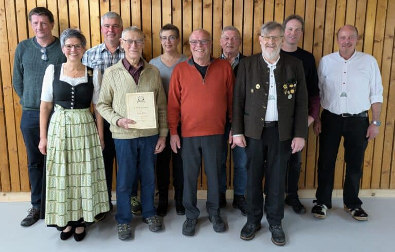 Gruppe von erwachsenen Menschen, die vor einer getäfelten Wand steht. Einer der Männer hält eine Ehrungsurkunde in der Hand.